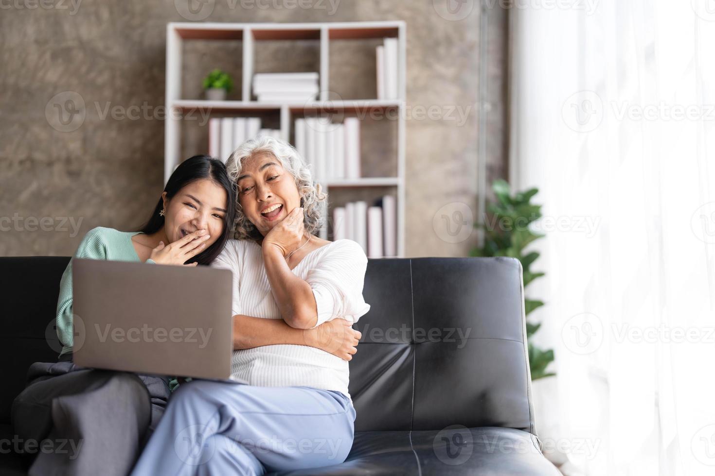 Mature mother grown up daughter sit on couch in living room hold on lap pc looking at screen watching movie film, using device make video call, shopping via e-commerce website, girl teach mom concept photo