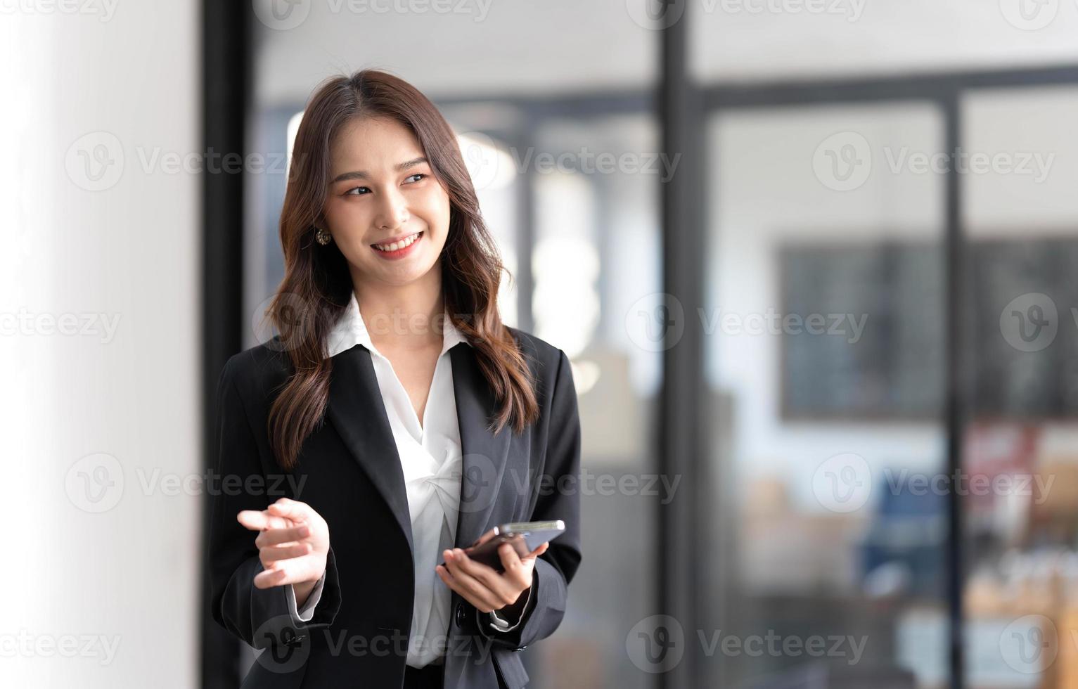 imagen de una joven empresaria asiática parada usando un teléfono móvil en la oficina. foto