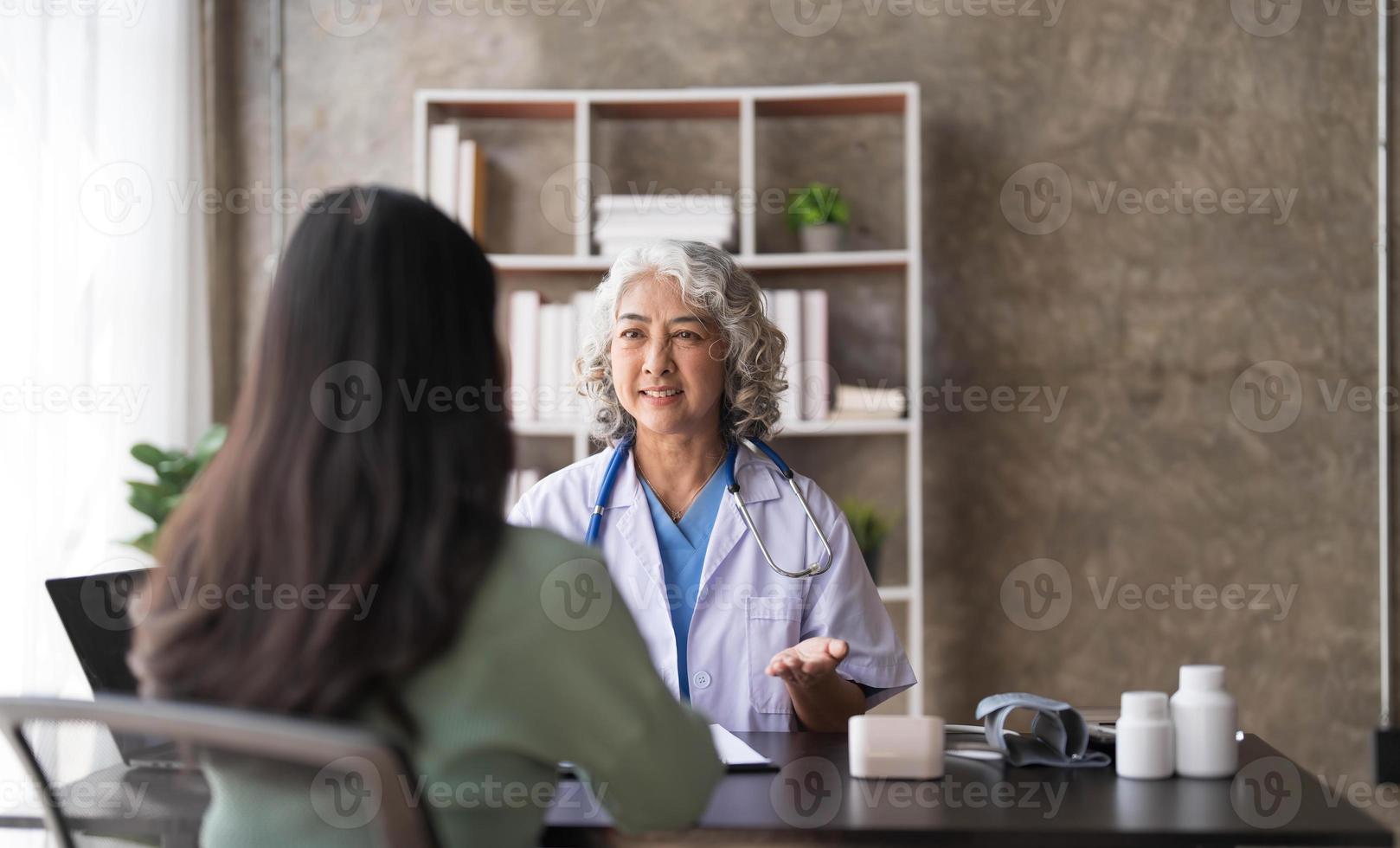 una doctora principal está leyendo el historial médico de una paciente y hablando con ella durante la consulta en una clínica de salud. médico en bata de laboratorio sentado detrás de una computadora portátil en la oficina del hospital. foto