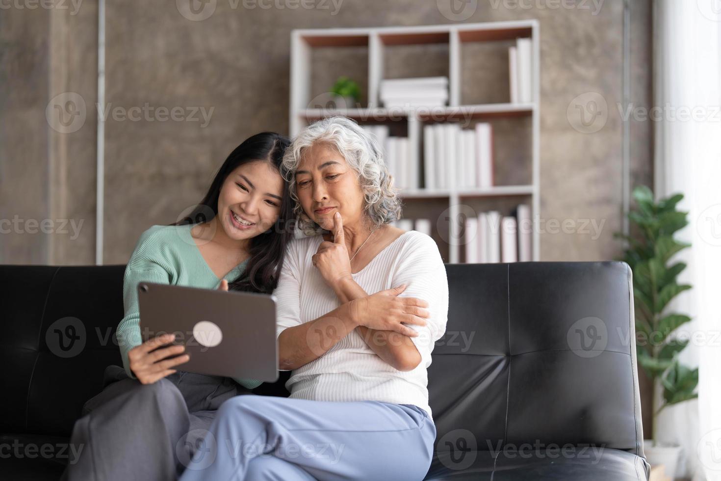 Mature mother grown up daughter sit on couch in living room hold on lap pc looking at screen watching movie film, using device make video call, shopping via e-commerce website, girl teach mom concept photo
