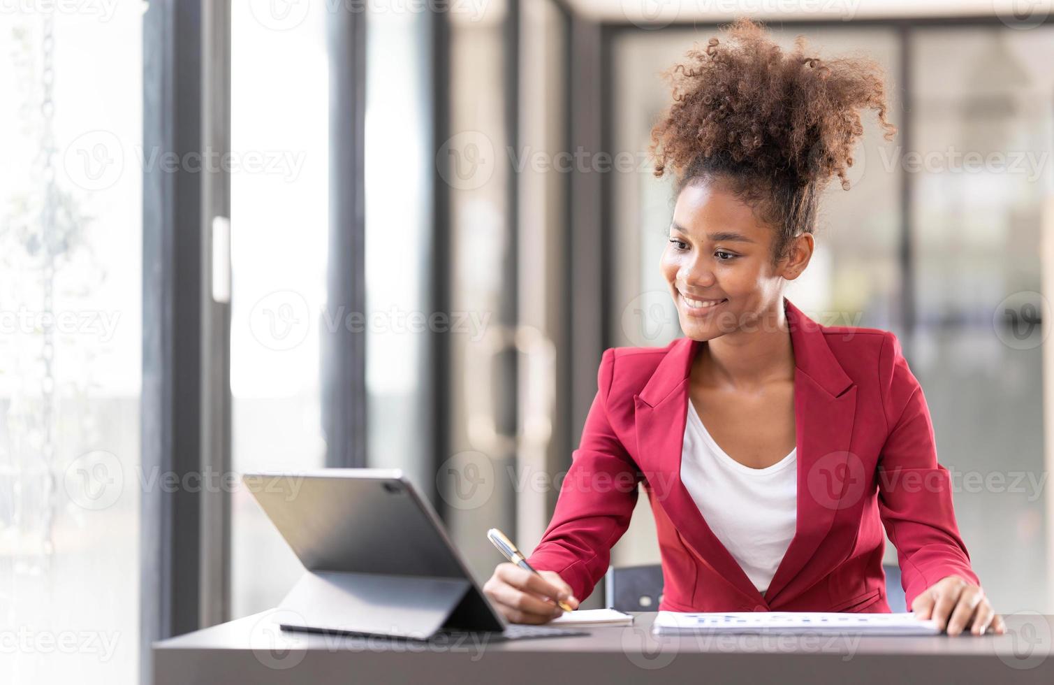 una joven empresaria asistente financiera afroamericana que usa una tableta digital y una computadora portátil mientras trabaja en un informe financiero. foto