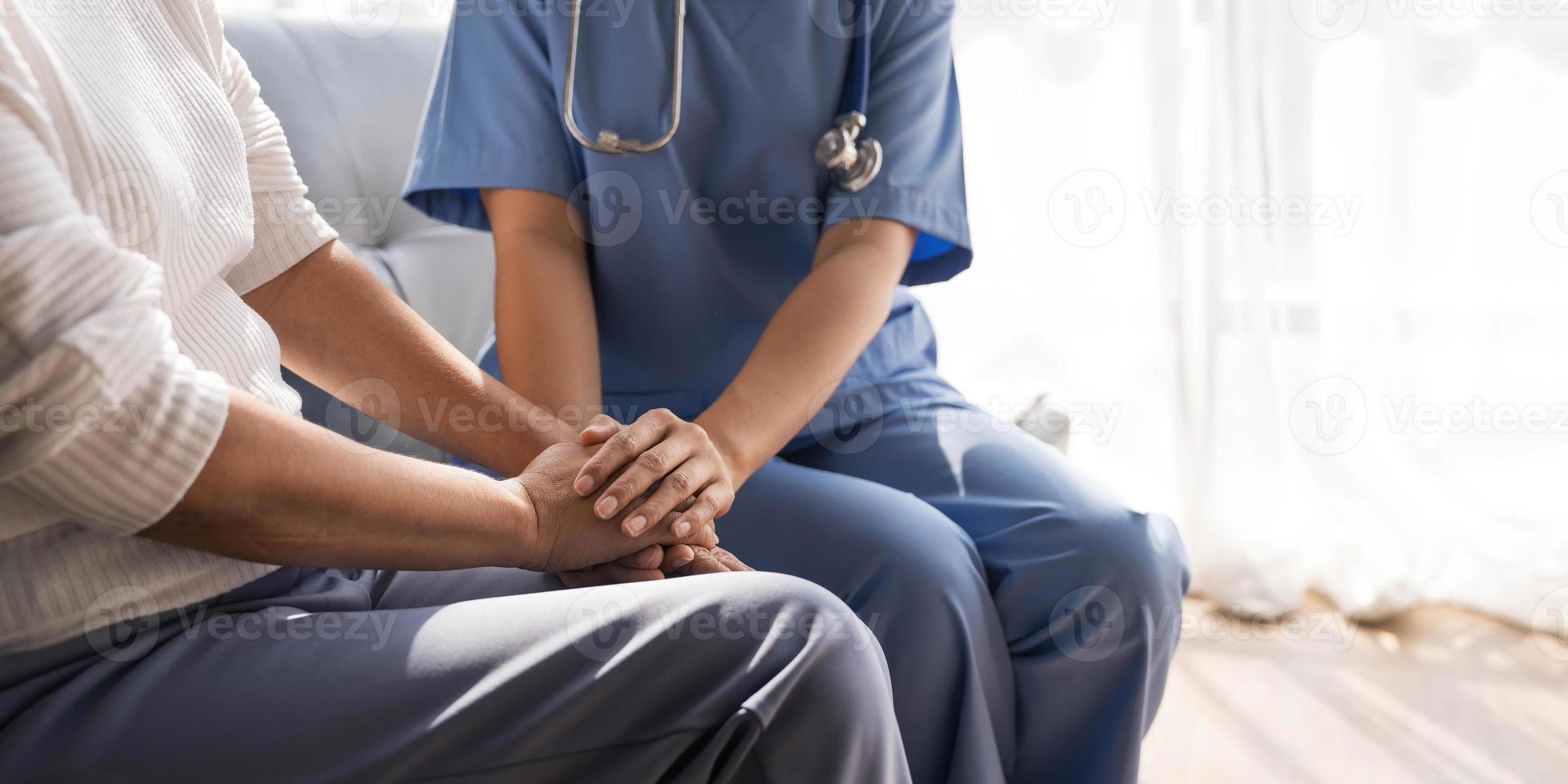 Closeup Happy patient is holding caregiver for a hand while spending time together. Elderly woman in nursing home and nurse. photo