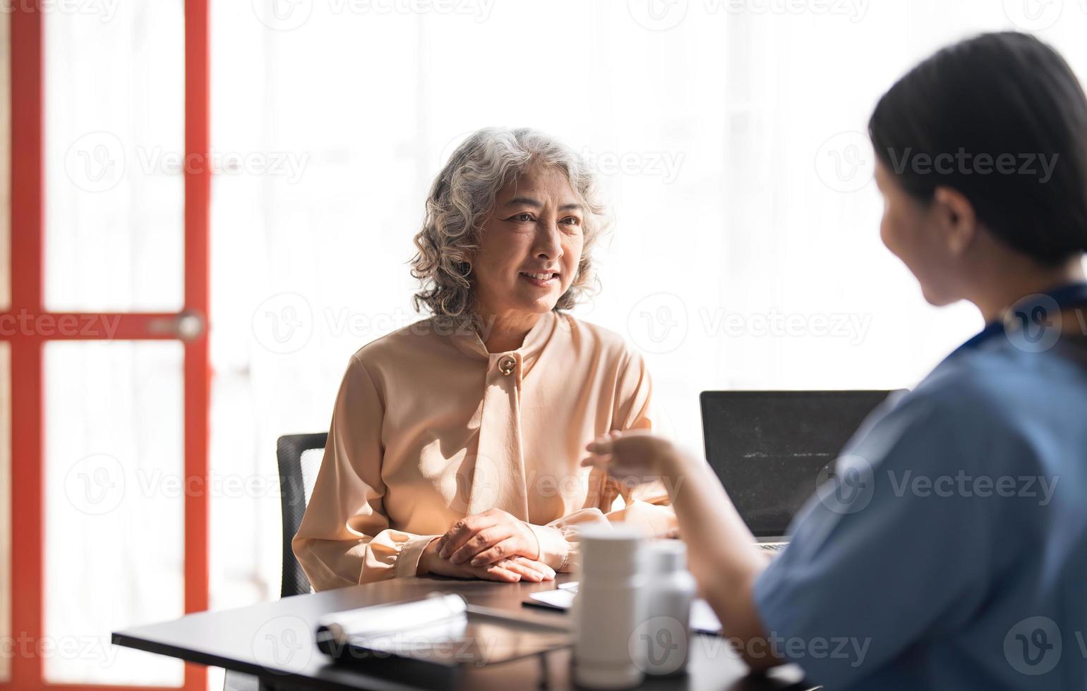 Asian Senior elderly female patient consult with physician nurse at nursing home care. Caregiver therapist pharmacist girl hold medicine pills bottle, explain prescription to older disabled guy photo