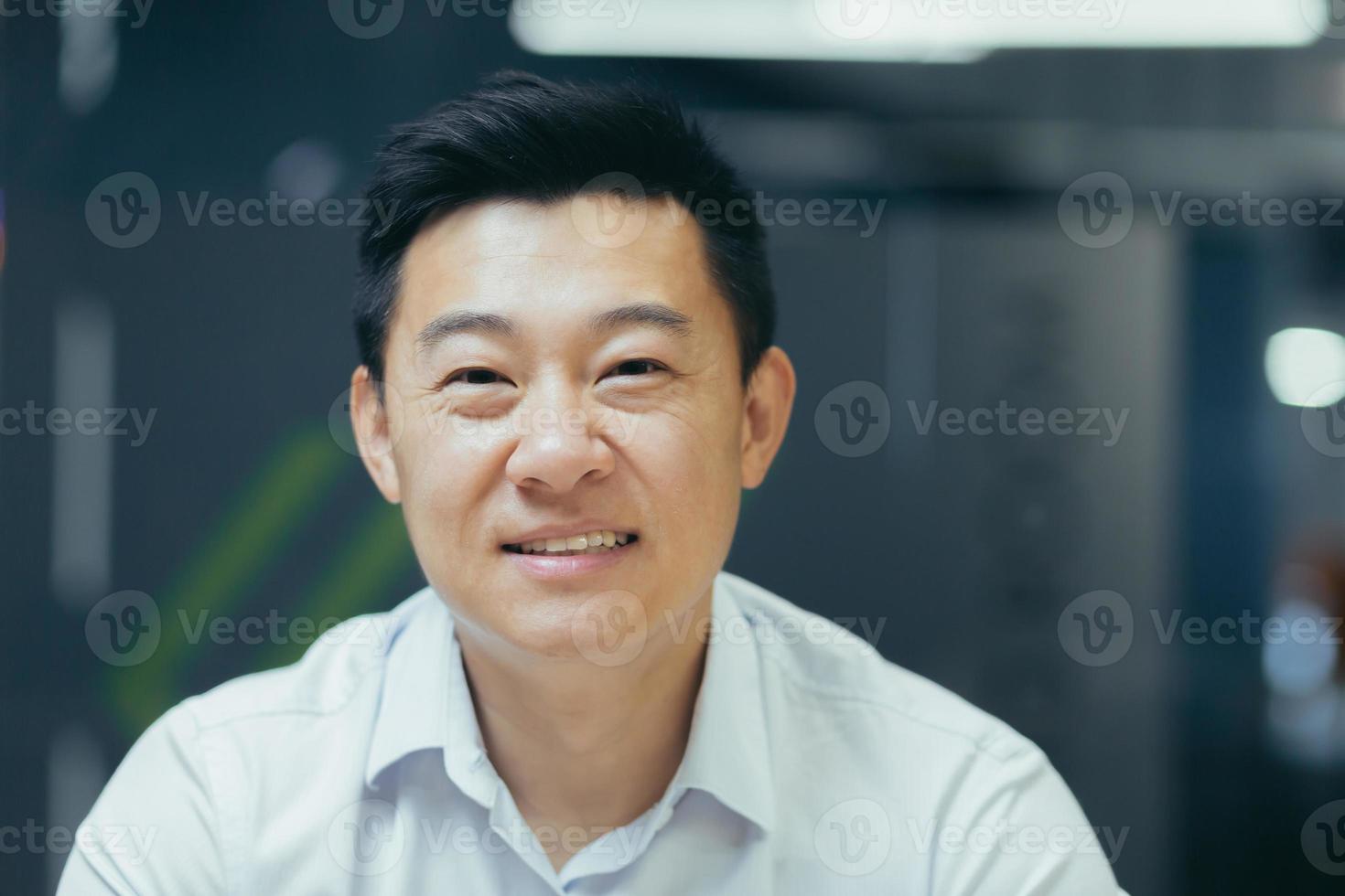 Close-up photo. Portrait of young handsome smiling Asian businessman in white shirt in modern office, photo