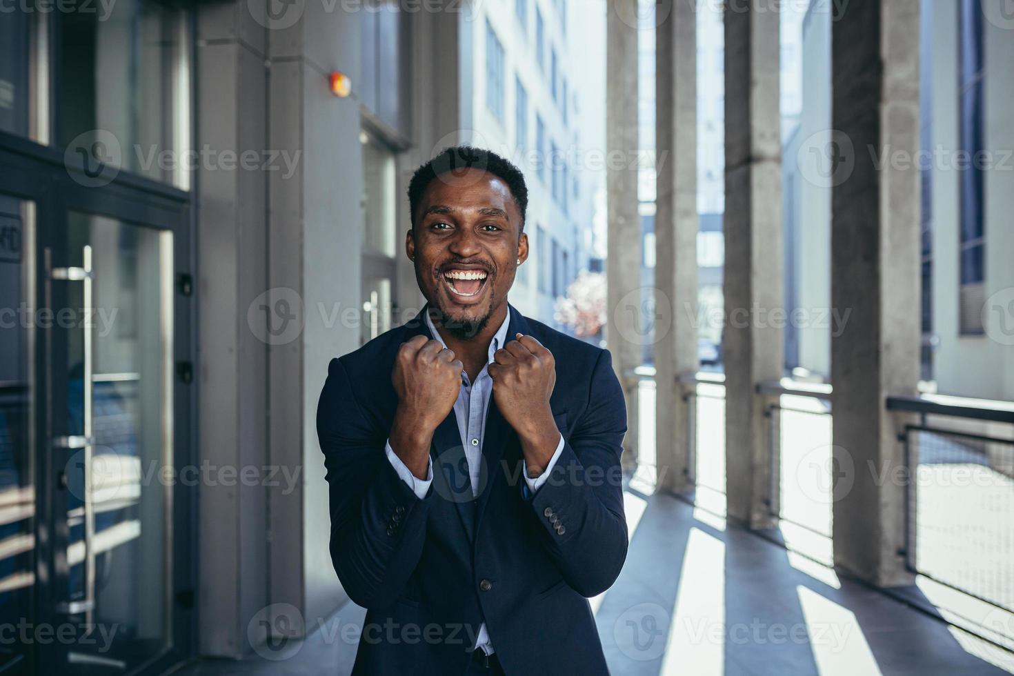 excited african american businessman rejoices in victory looking at camera while standing outside photo