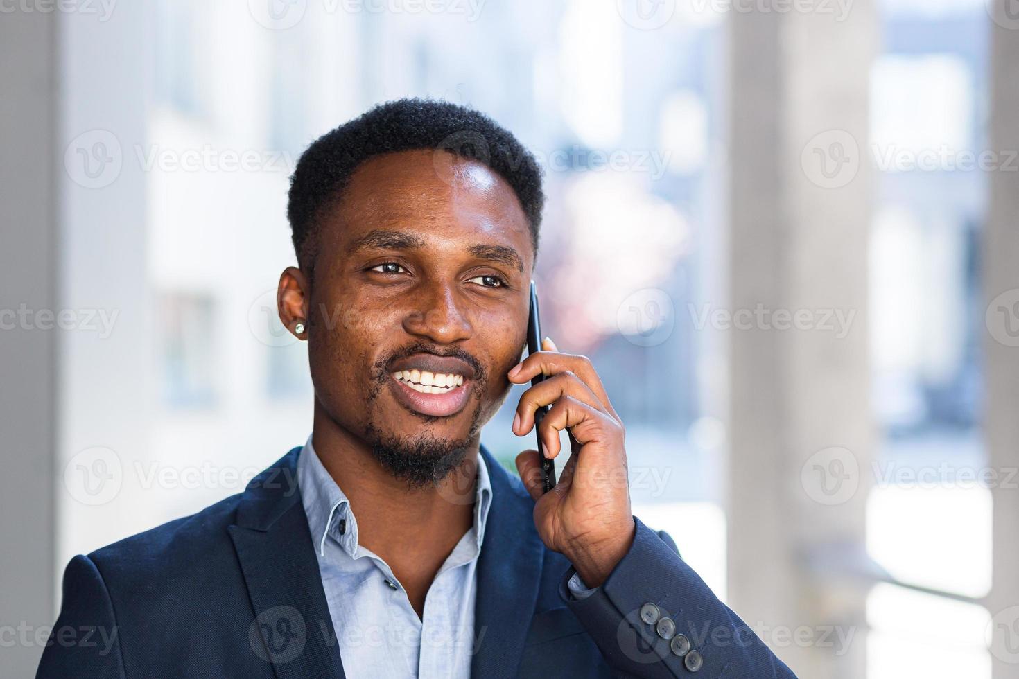 Cierra el retrato de un hombre de negocios africano hablando por teléfono y sonriendo por el éxito. foto