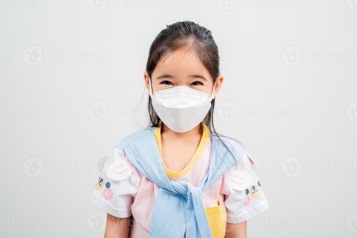 Asian little child girl wearing respirator mask to protect coronavirus outbreak and pointing hand to blank background, New virus Covid-19 photo