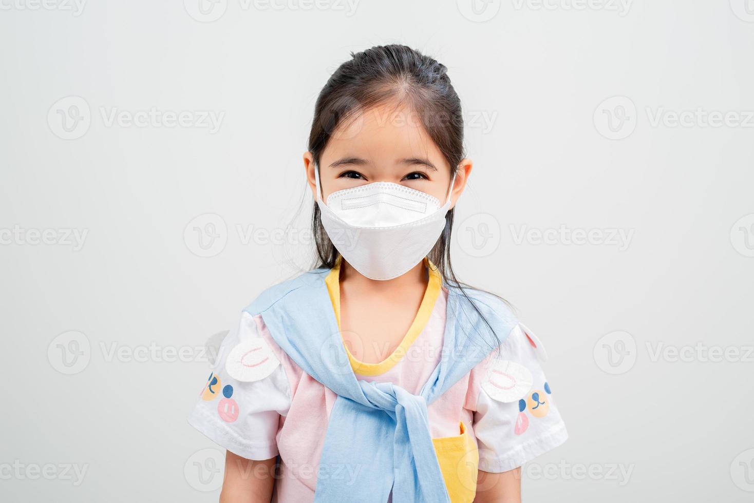 niña asiática con mascarilla respiratoria para proteger el brote de coronavirus y apuntando con la mano al fondo en blanco, nuevo virus covid-19 foto