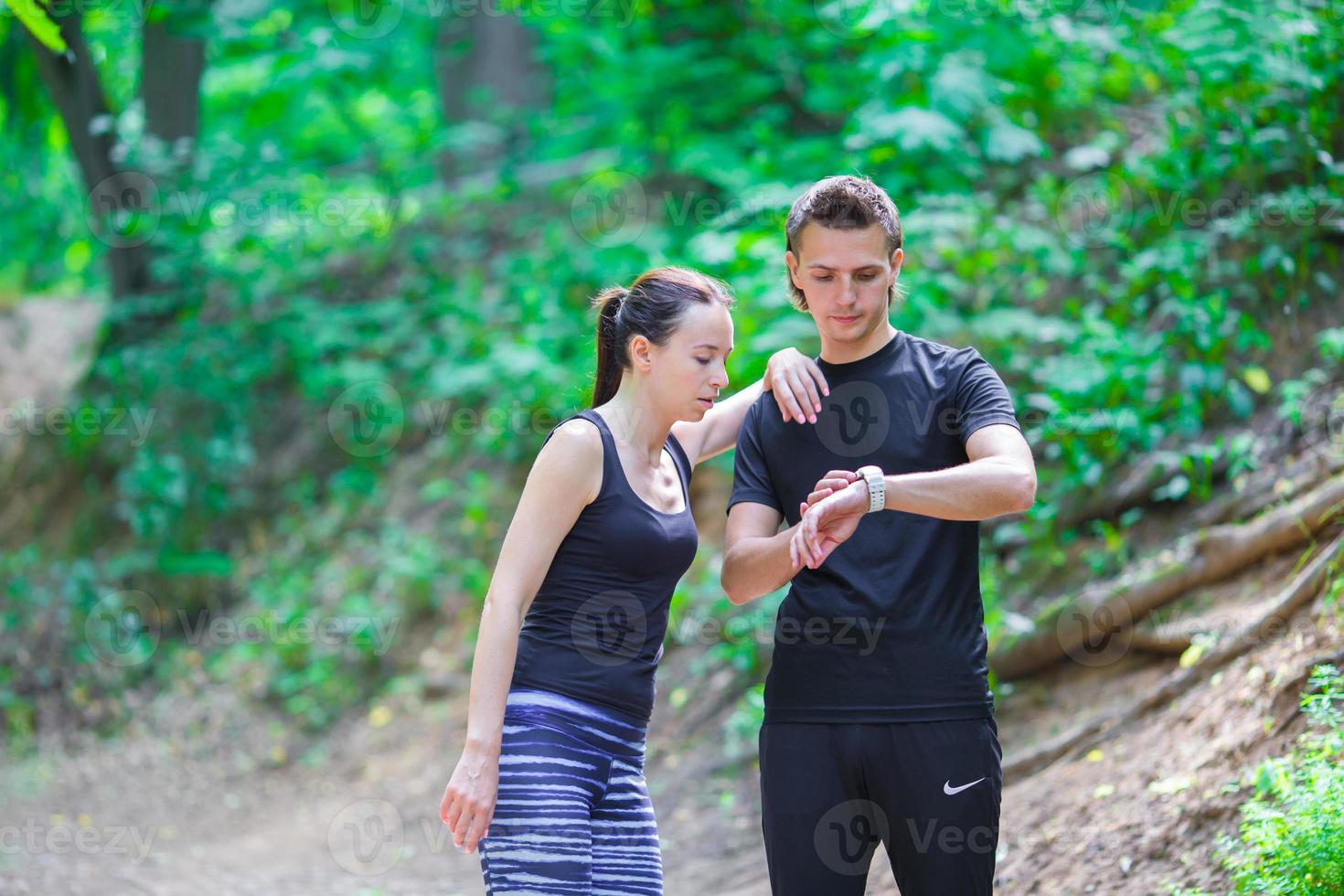 Young active couple looking at smart watch heart rate monitor having break while running at forest photo
