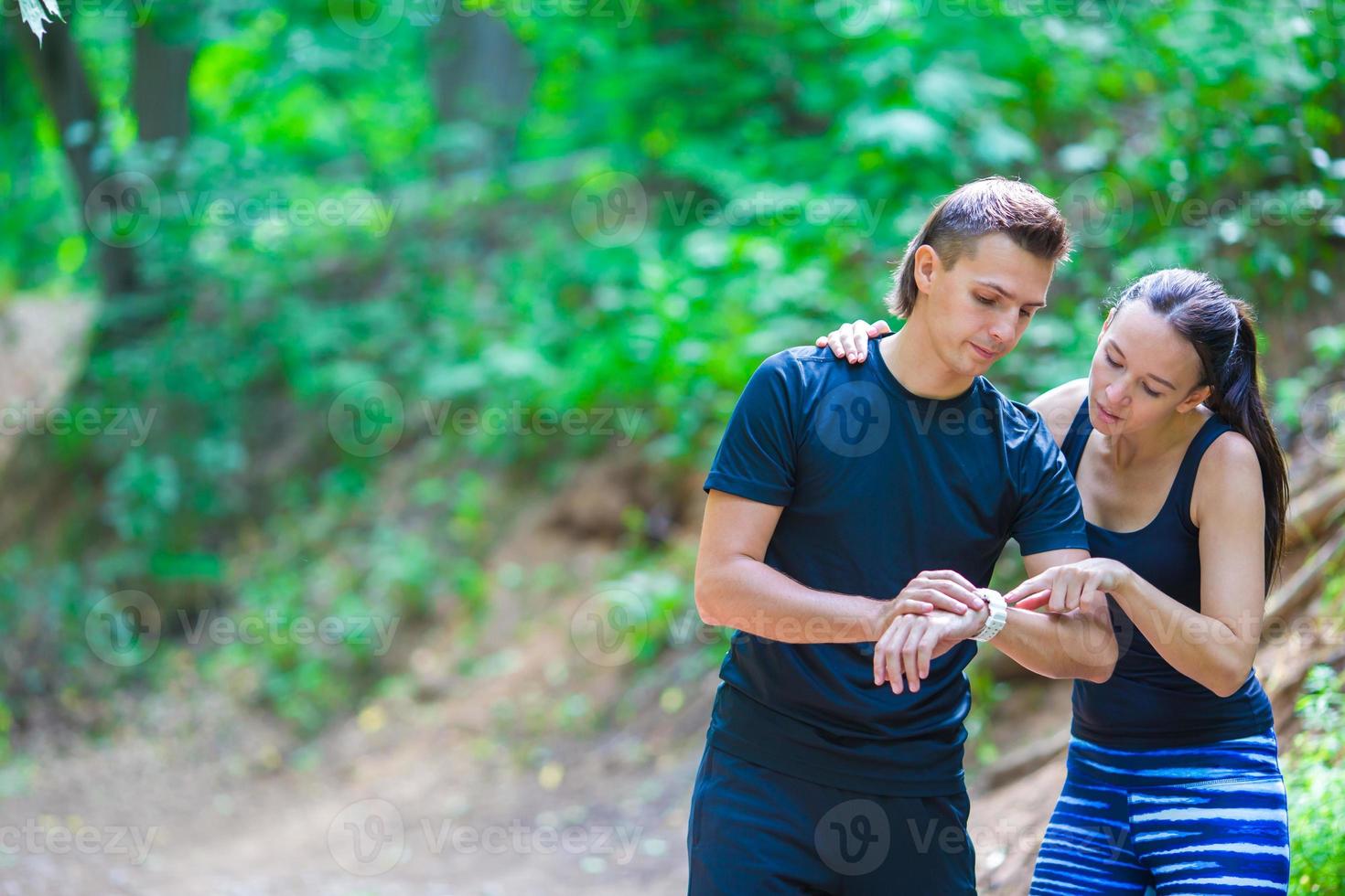 Young active couple looking at smart watch heart rate monitor having break while running at forest photo