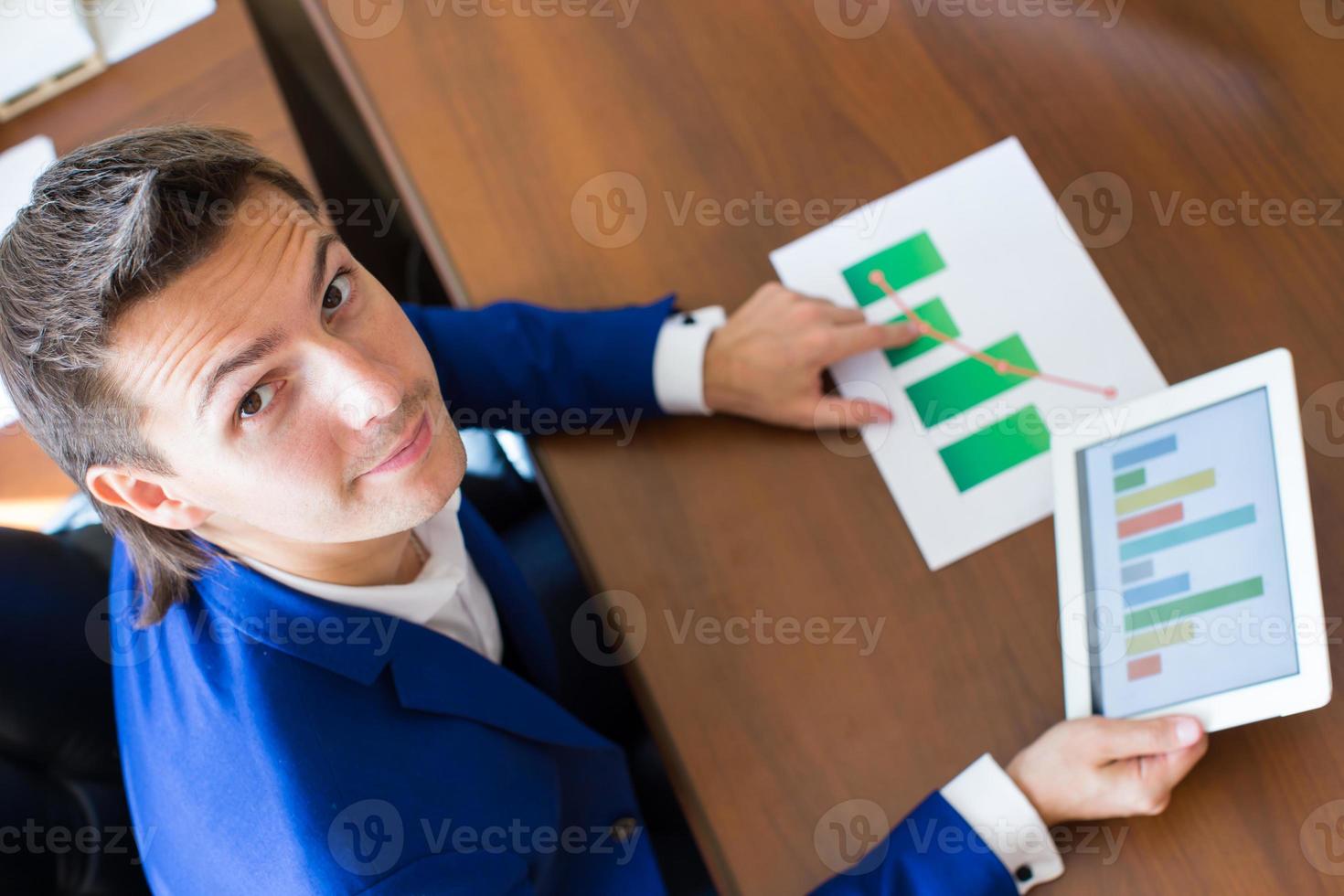 joven hombre de negocios que trabaja con una tableta, documentos y gráficos en su oficina foto