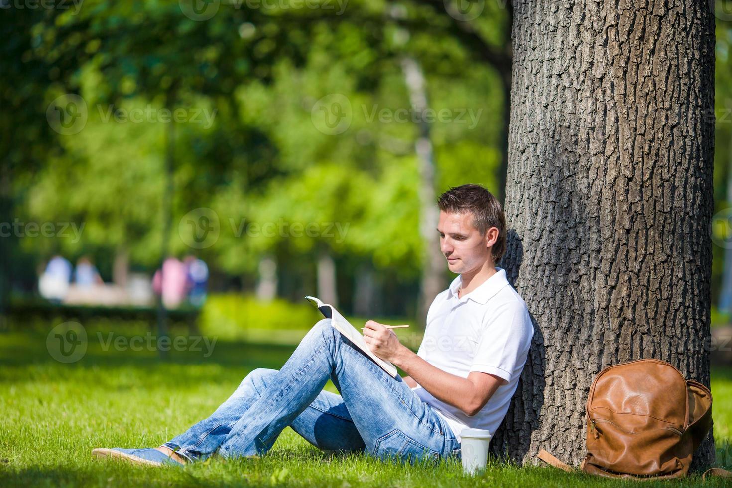 Young man relaxing near tree with coffee reading a book photo