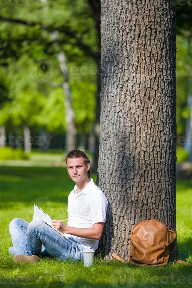 Young man relaxing near tree with coffee reading a book photo