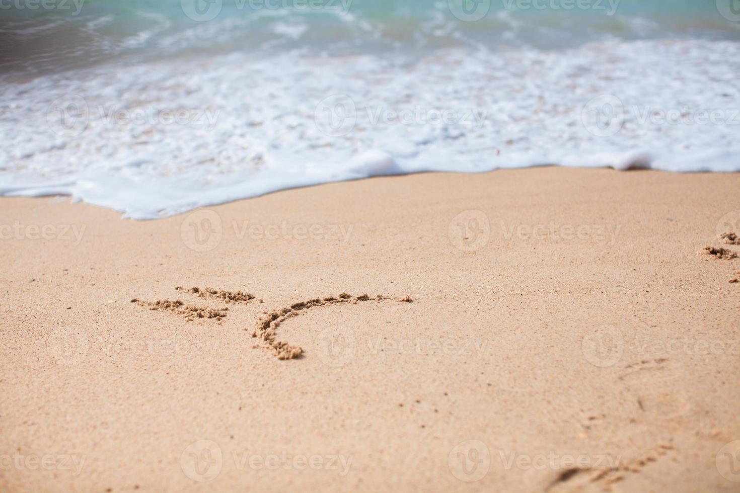 Sad smile drawing on the sand at tropical beach photo