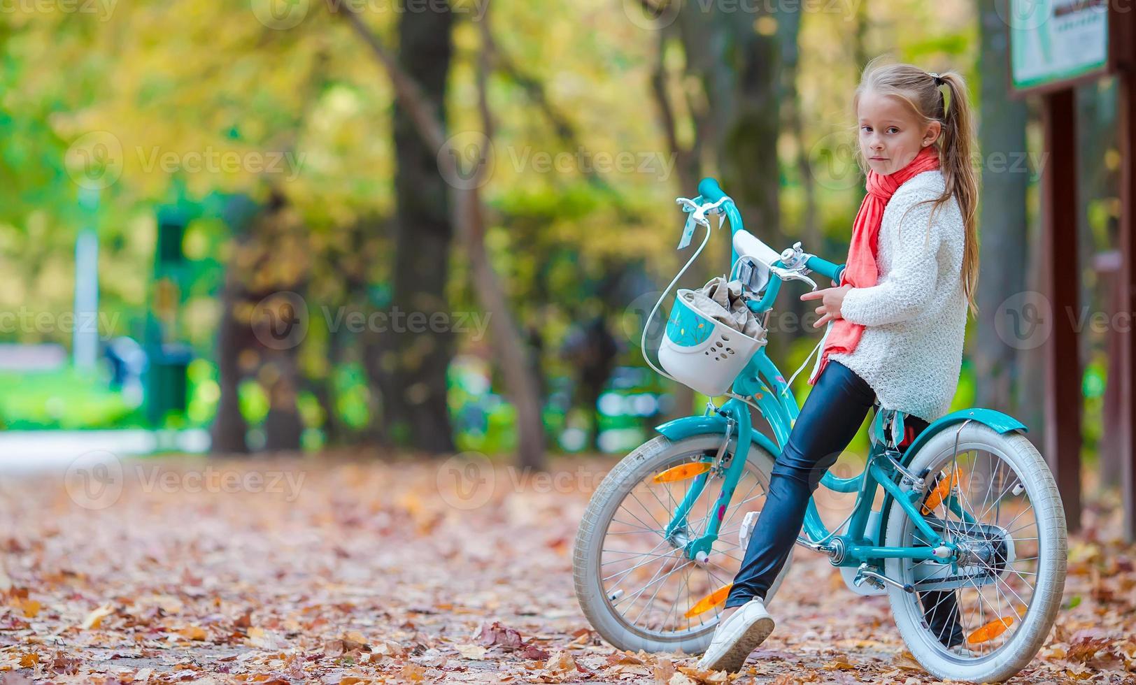 Adorable girl riding a bike at beautiful autumn day outdoors photo