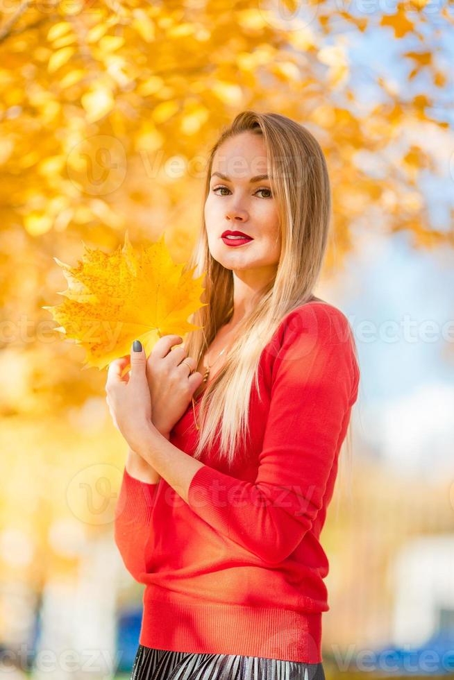 Fall concept - beautiful woman drinking coffee in autumn park under fall foliage photo