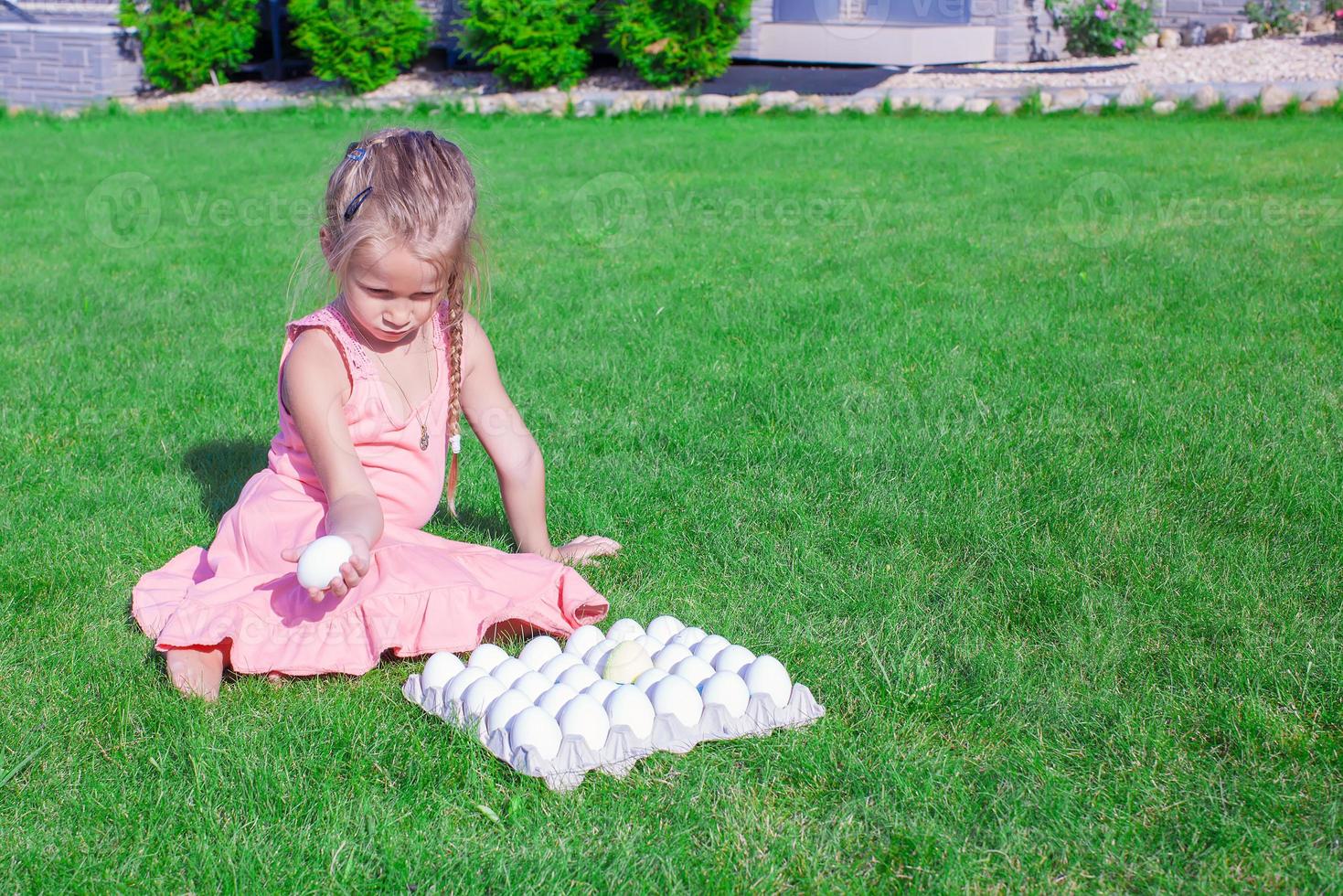 adorable niña sosteniendo un huevo de pascua blanco en su jardín foto