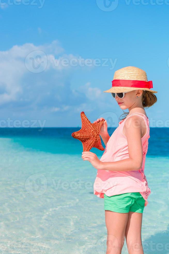 adorable niña con estrellas de mar en una playa blanca y vacía foto