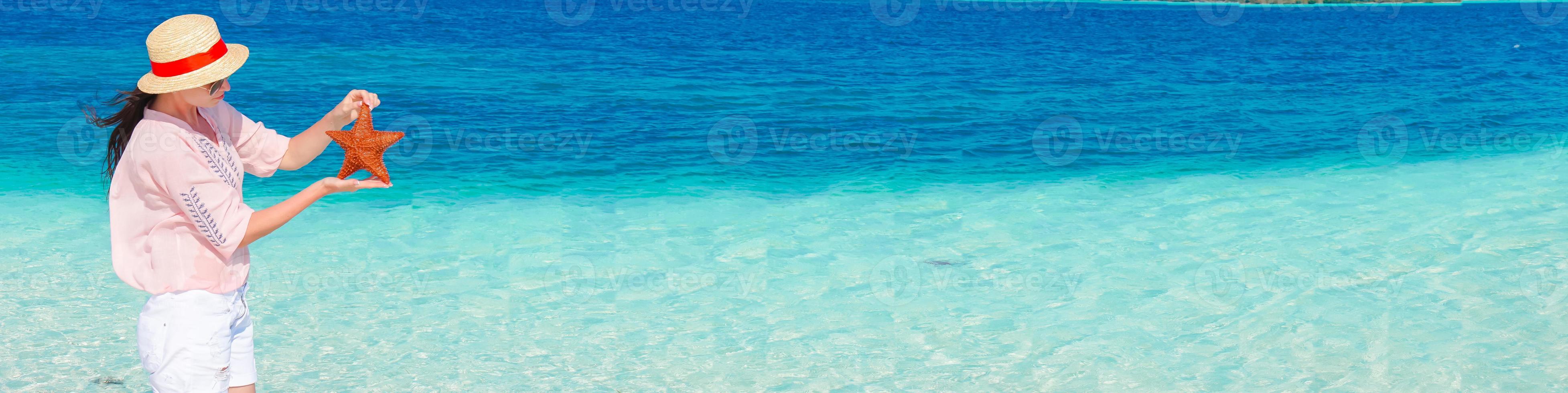 Panorama of young woman with starfish on white beach in the nature reserve photo