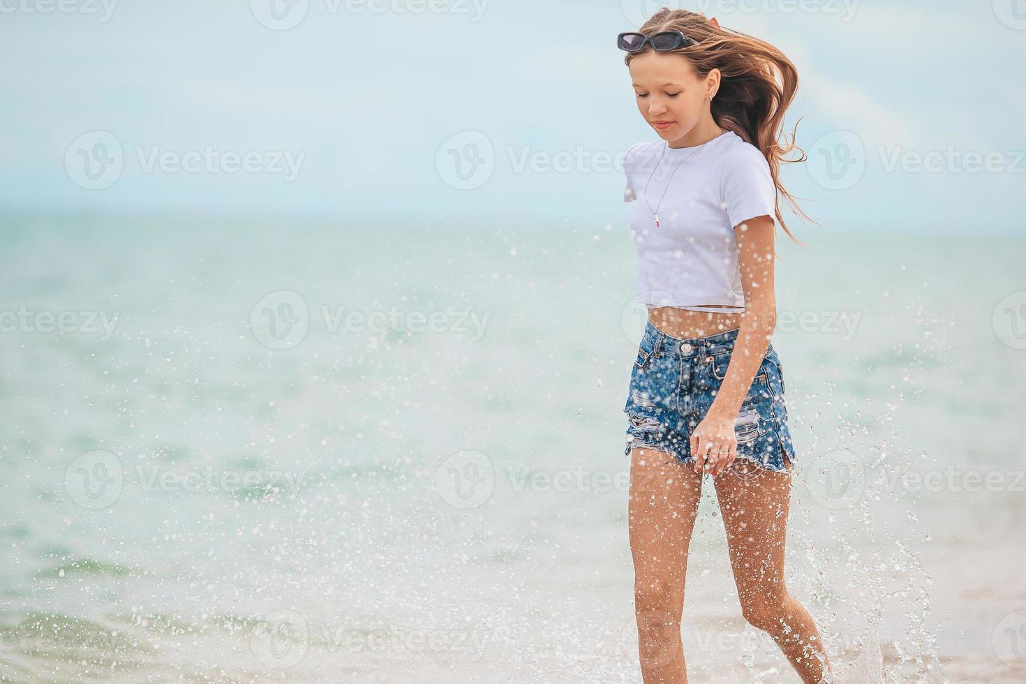 Little happy girl splashing and running in clear turquoise water photo