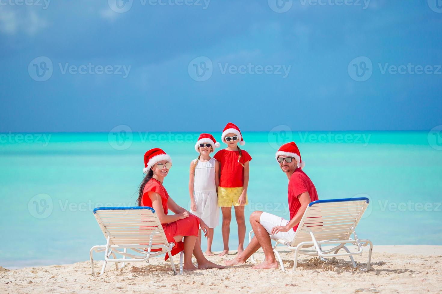 Happy family of four on beach in red Santa hats photo