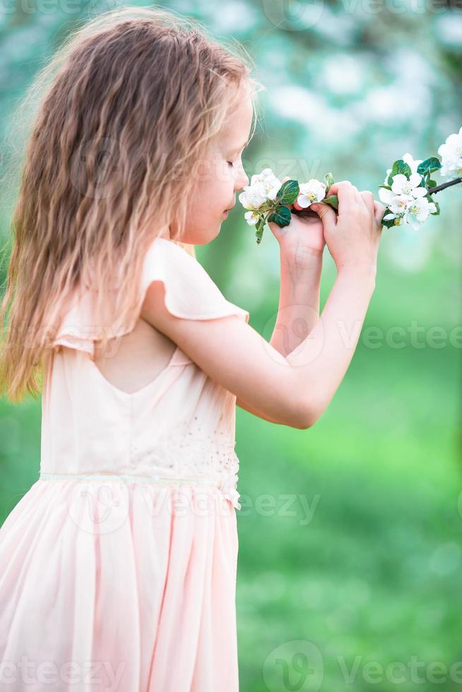 Little beautiful girl enjoying smell in a flowering spring garden photo