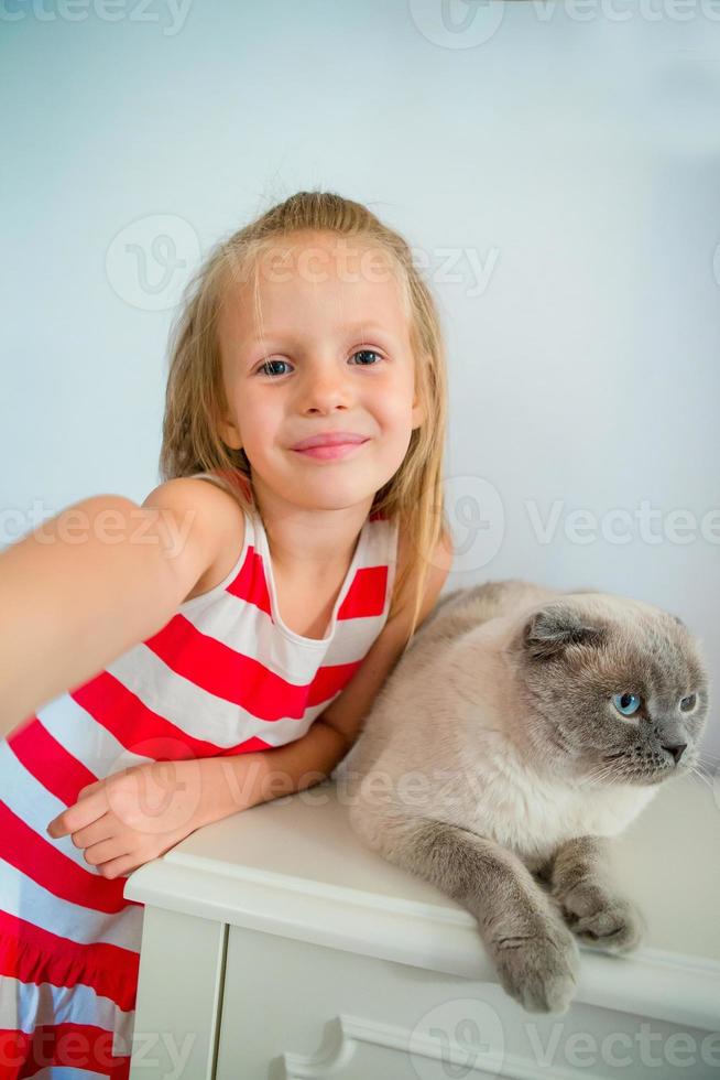 Cute little girl kissing her pet cat at home. Love between kid and pet photo