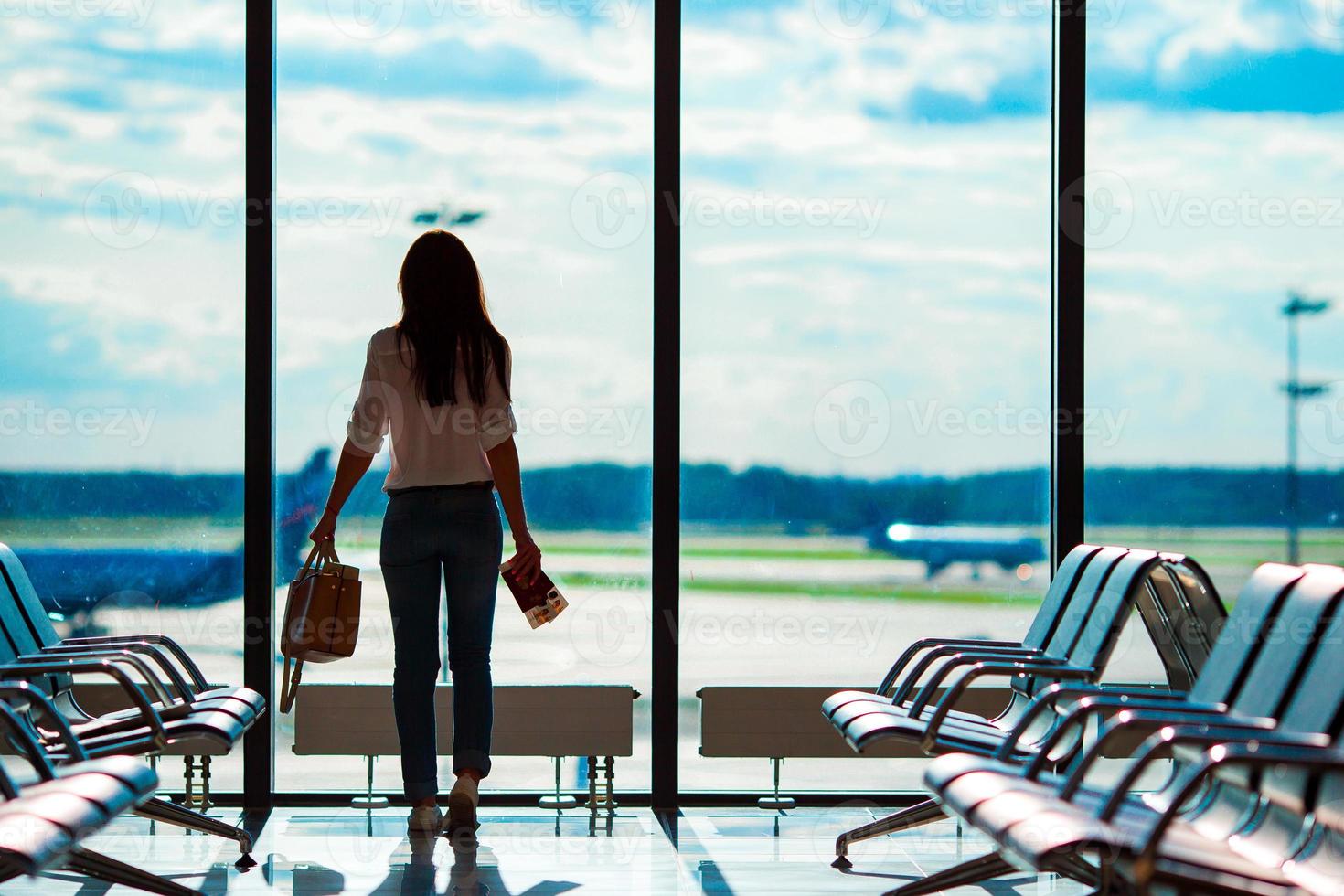 mujer joven en el aeropuerto internacional con su gran ventana de fondo de equipaje. Pasajero de línea aérea en un salón del aeropuerto esperando aviones de vuelo foto