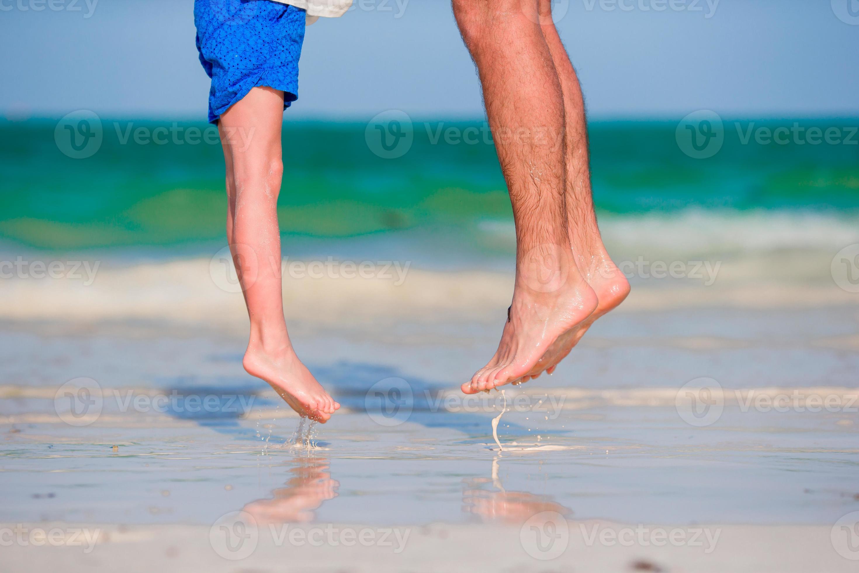 Closeup kid and adult feet jumping in shallow water on white sandy