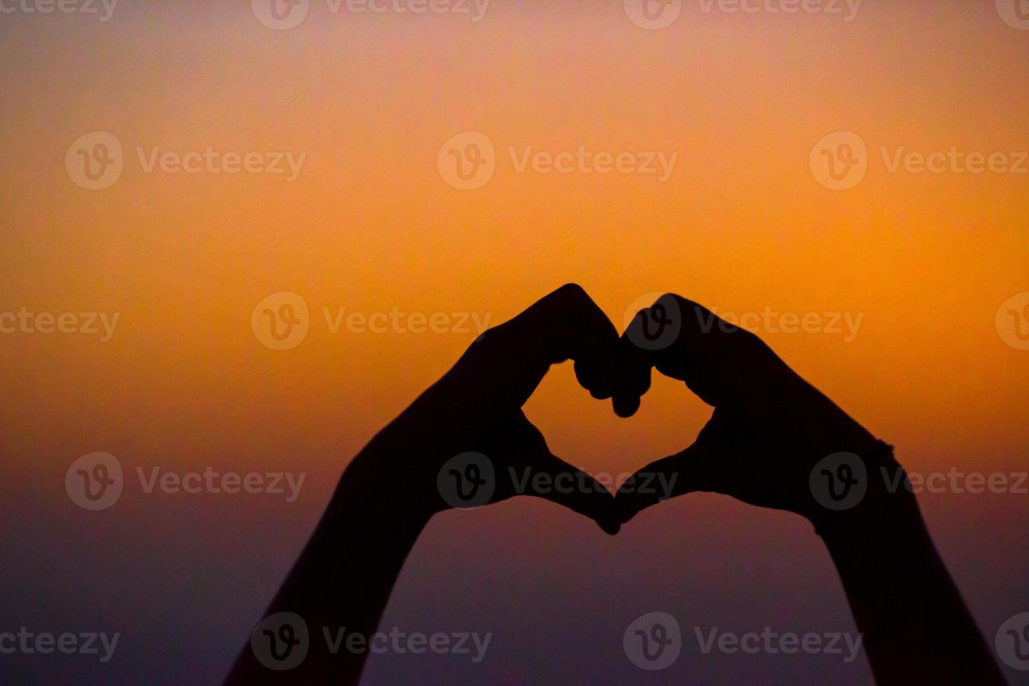 Silhouette of heart made hands at sunset photo