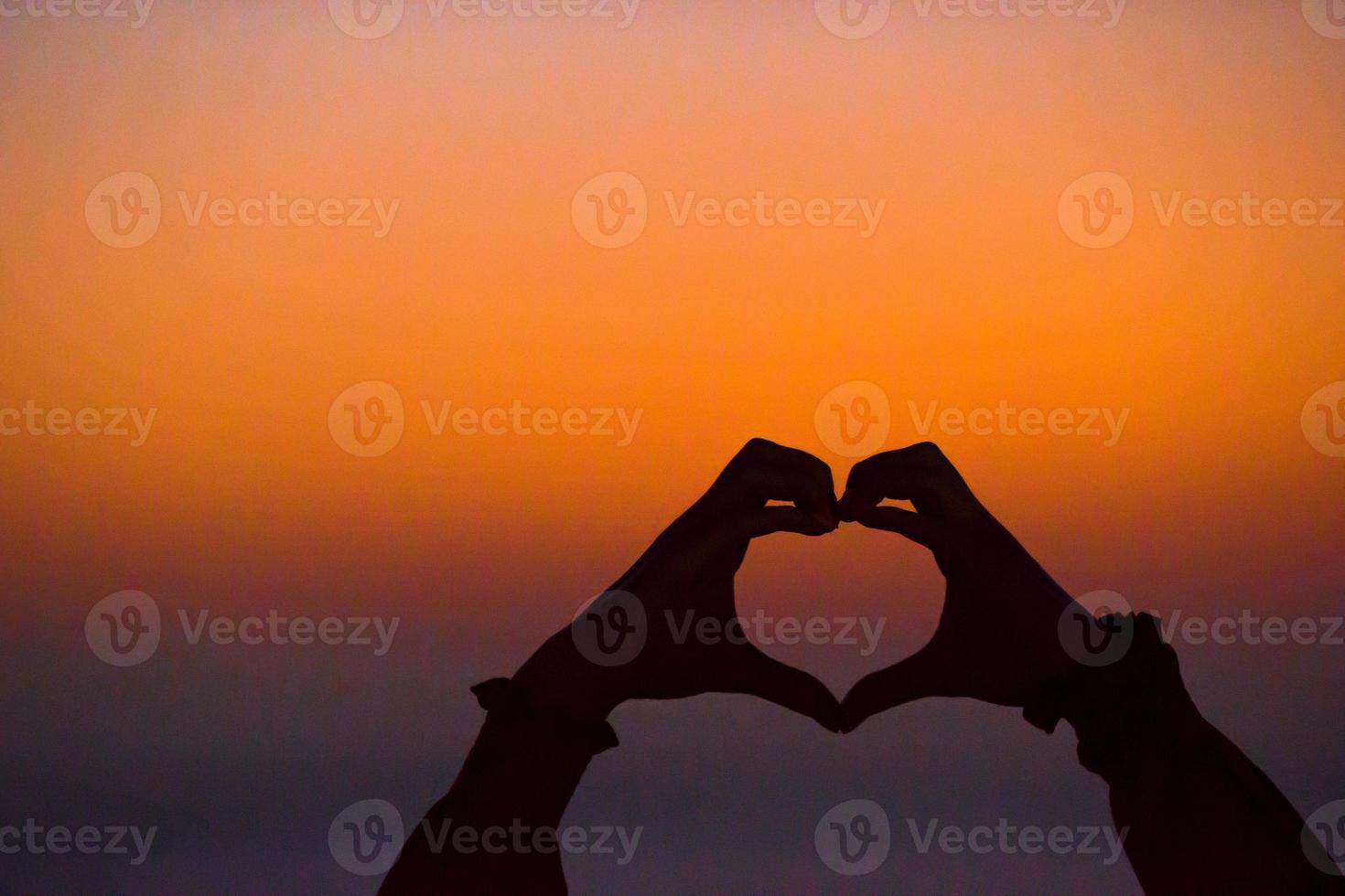 Silhouette of heart made hands at sunset photo