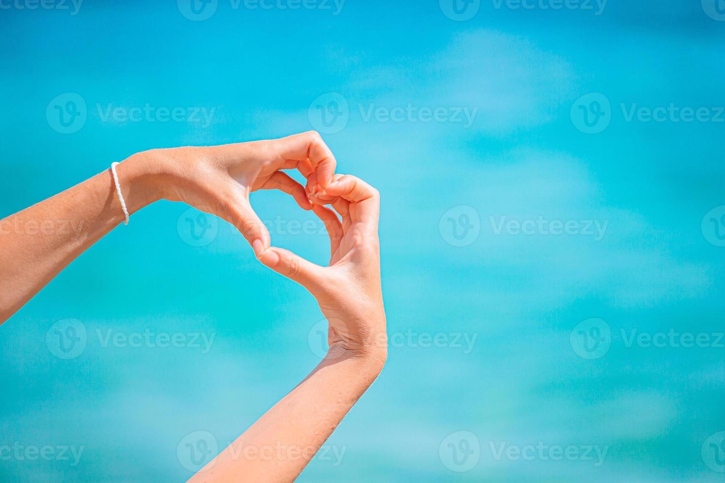 Female hands in the form of heart against the turquoise sea photo