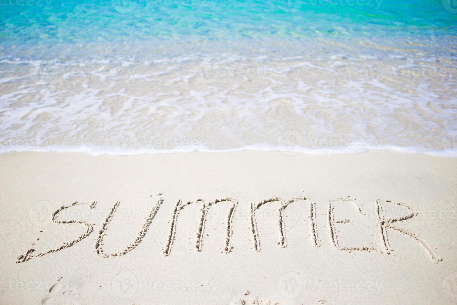 Word Summer handwritten on sandy beach with soft ocean wave on background photo