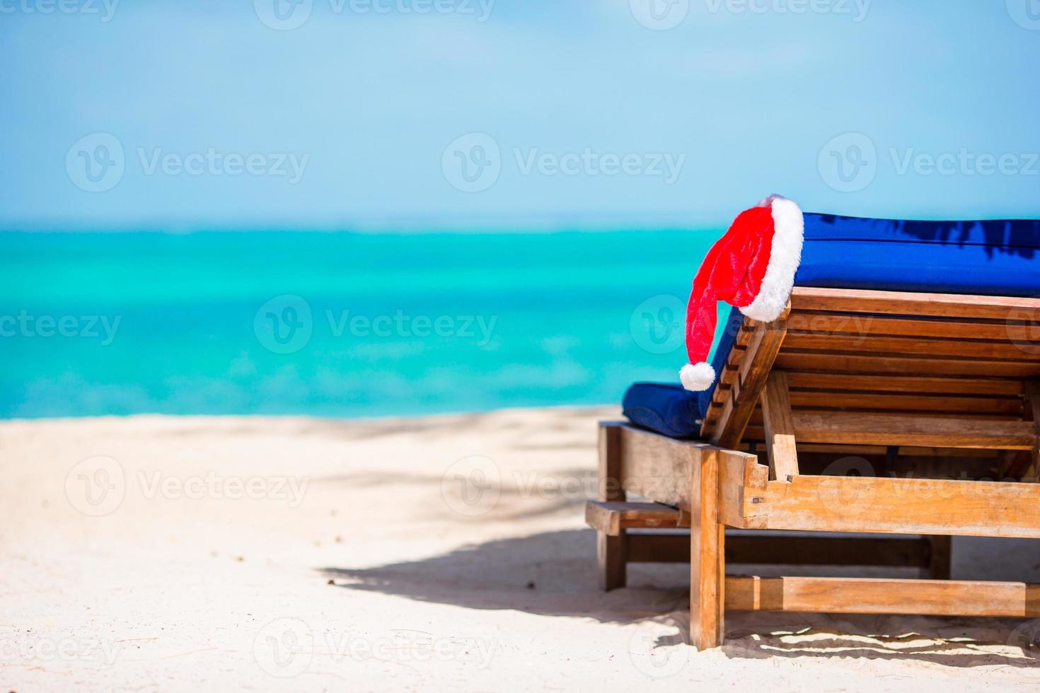 Santa Claus Hat on beach lounger with turquoise sea water and white sand. Christmas vacation concept photo