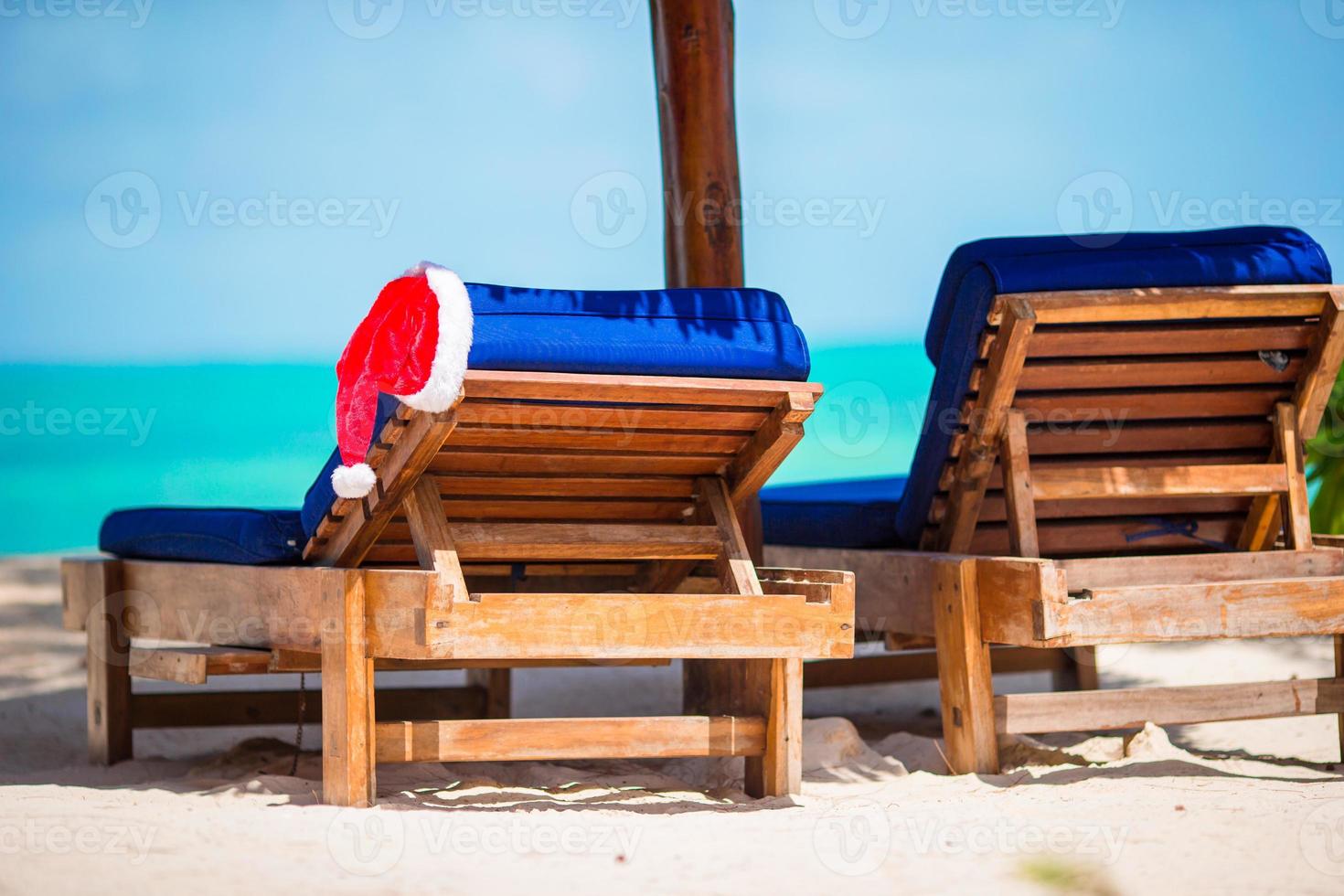 Santa Claus Hat on beach lounger with turquoise sea water and white sand. Christmas vacation concept photo