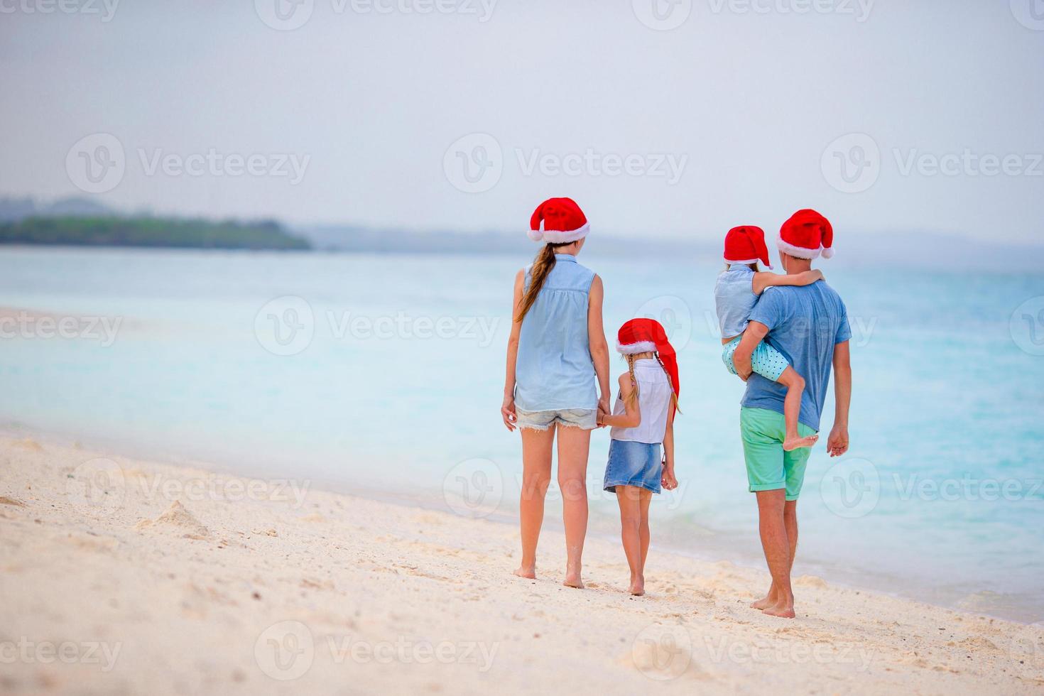 feliz hermosa familia con sombreros rojos de santa en la playa tropical celebrando la navidad foto