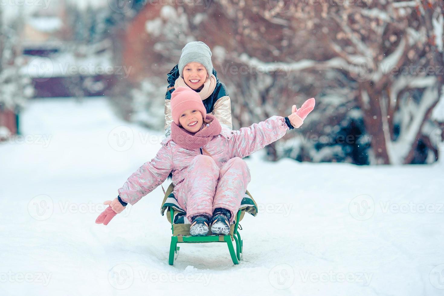 Adorable little happy girls sledding in winter snowy day. photo