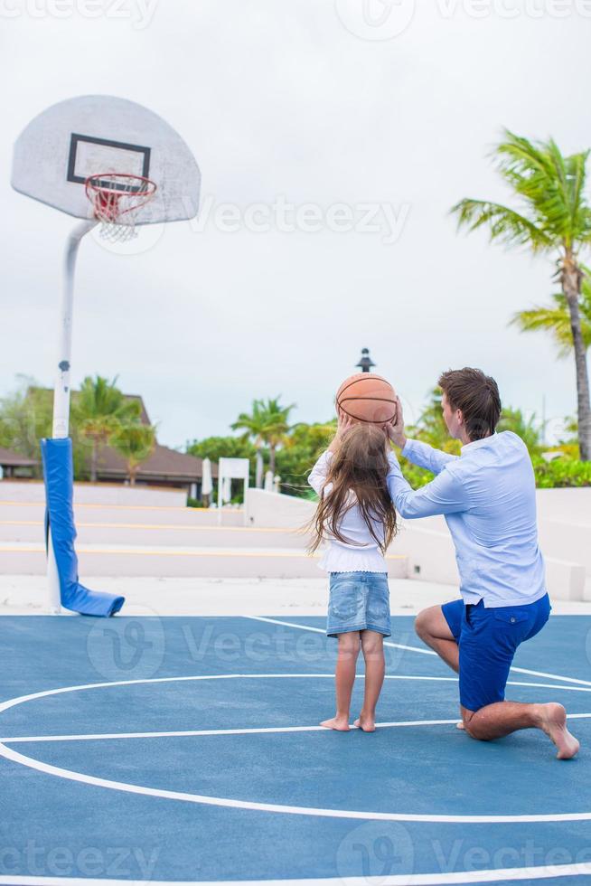 Young man and little girl playing basketball outside at exotic resort photo