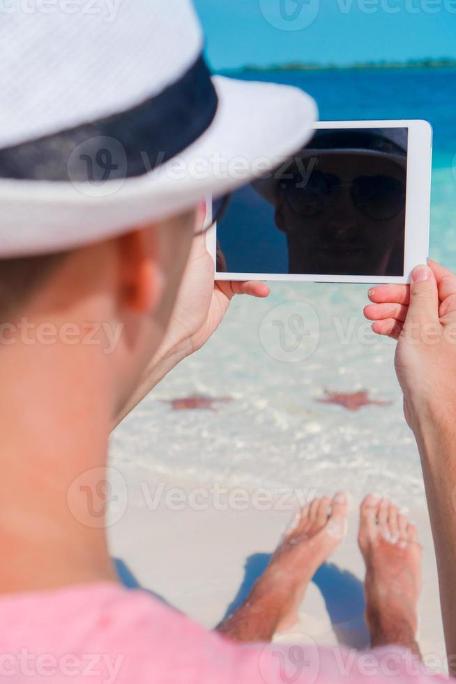 Young man with laptop on the background of turquoise ocean at tropical beach photo