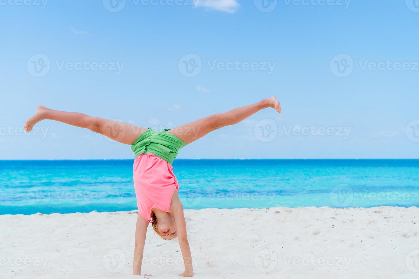 Active little girl at beach having a lot of fun. Sporty kid makes the wheel on the seashore photo