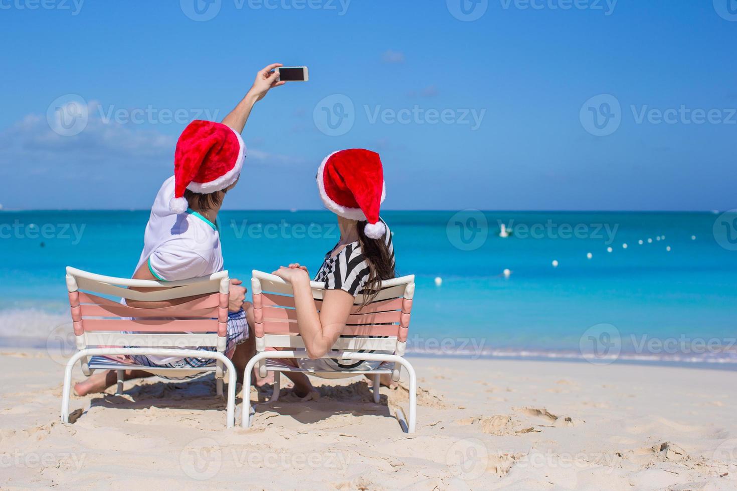 joven pareja feliz con sombreros rojos de santa tomando una foto en el teléfono celular