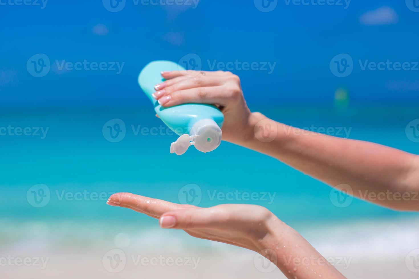 Woman hands putting sunscreen from a suncream bottle photo