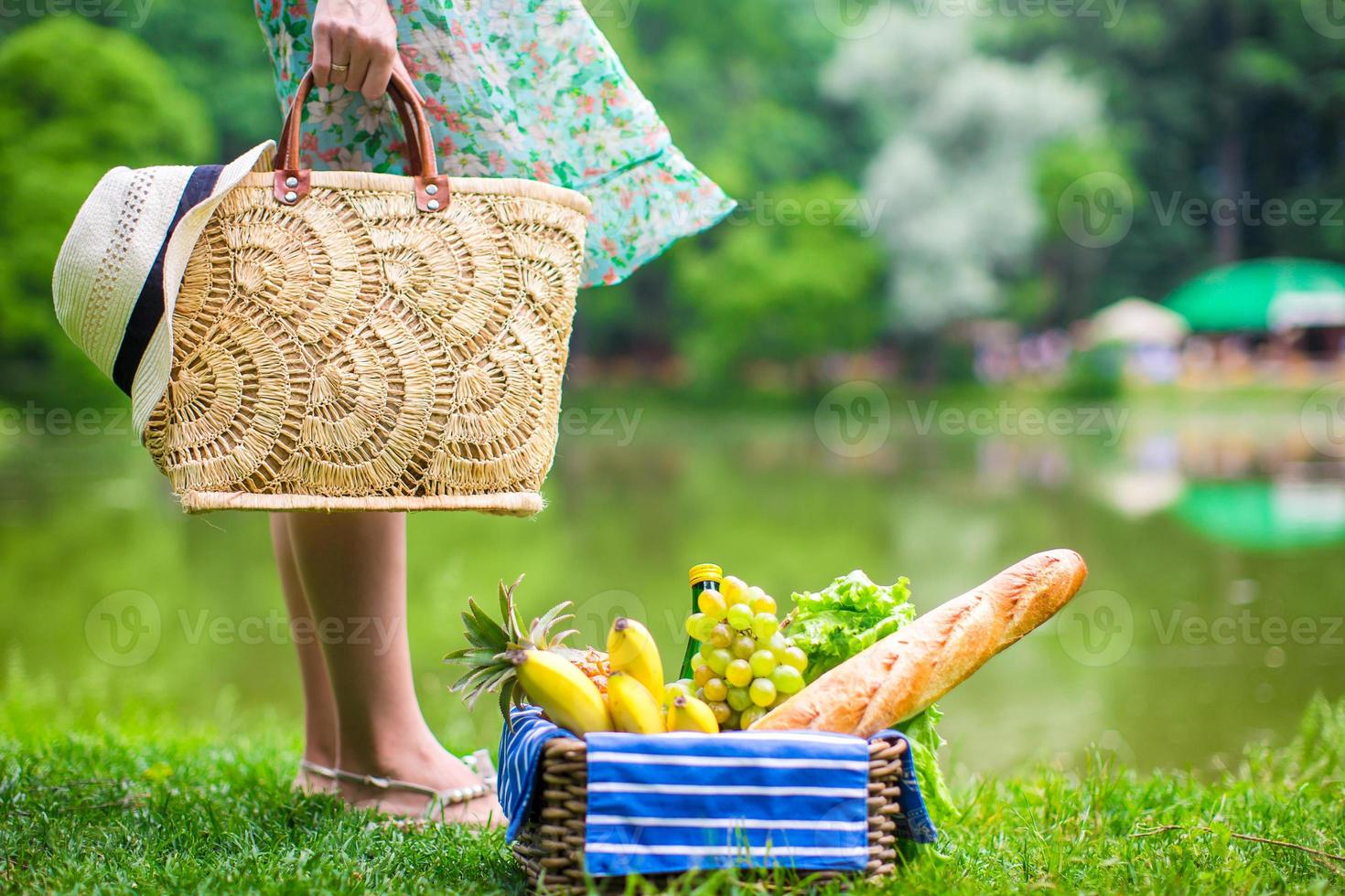 Picnic basket with fruits, bread and hat on straw bag photo