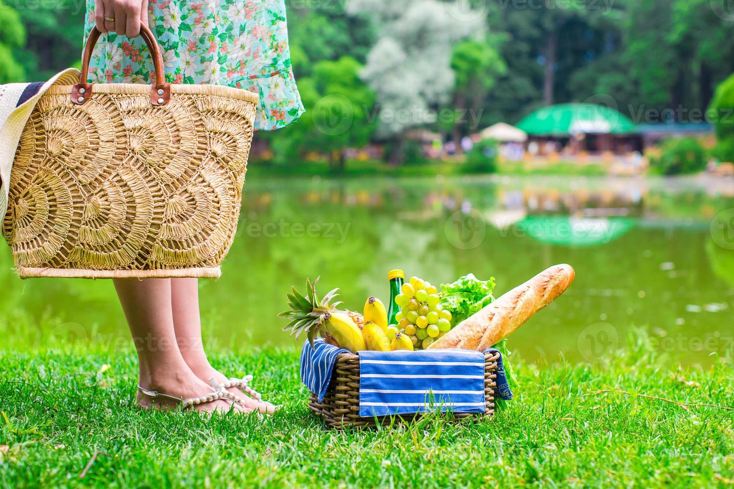 Picnic basket with fruits, bread and hat on straw bag photo