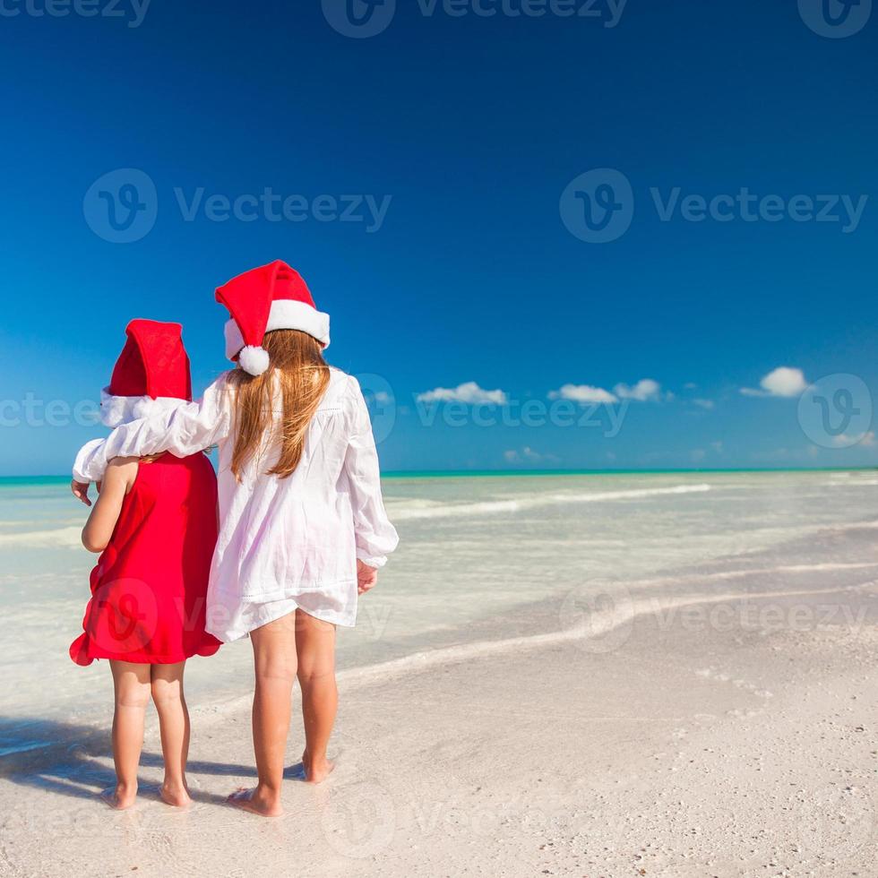 niñas adorables con sombreros de santa durante las vacaciones en la playa foto