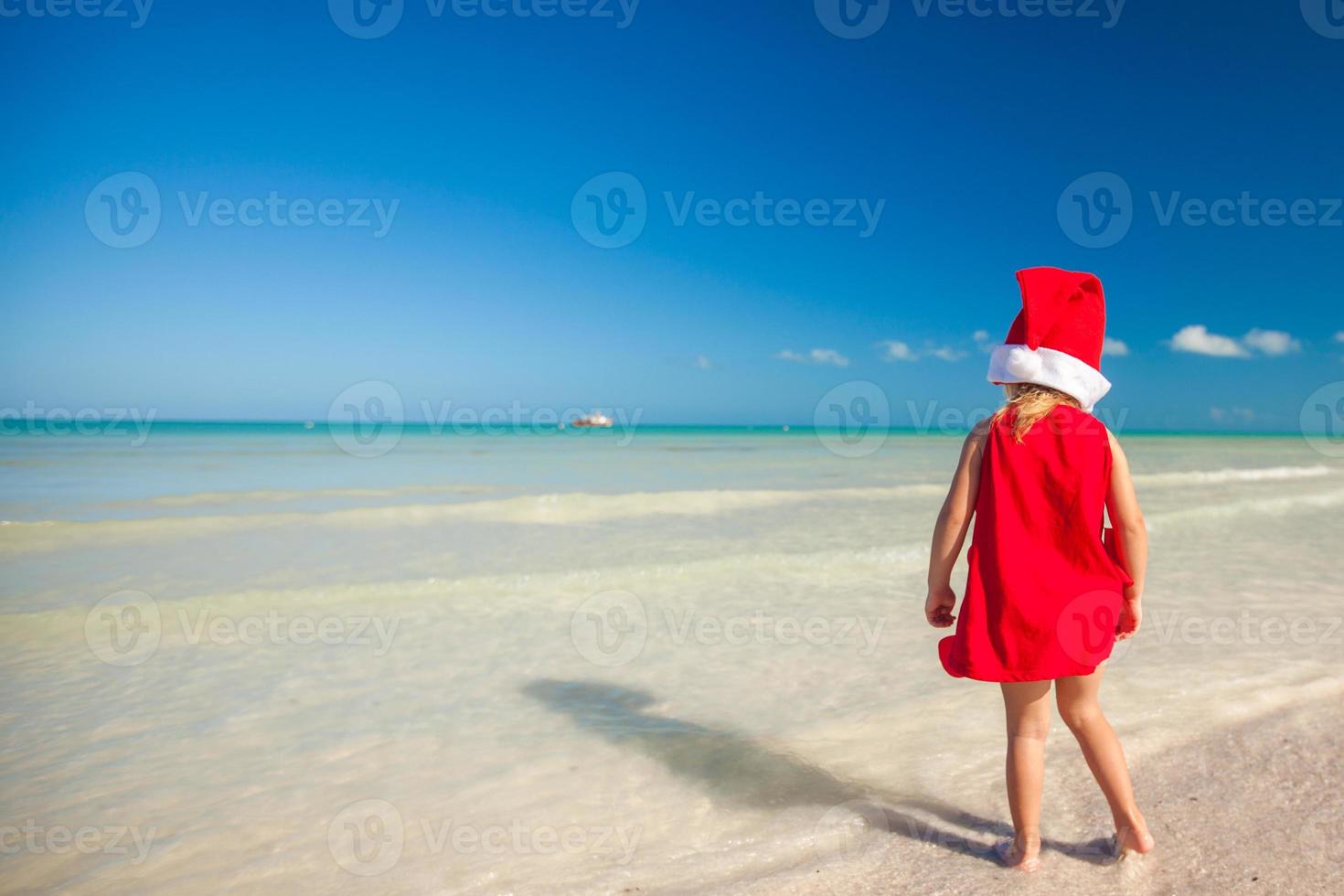 Little adorable girl in red Santa hat at tropical beach photo