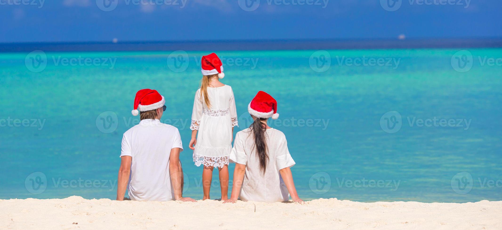 Happy family of three in Santa Hats on beach photo