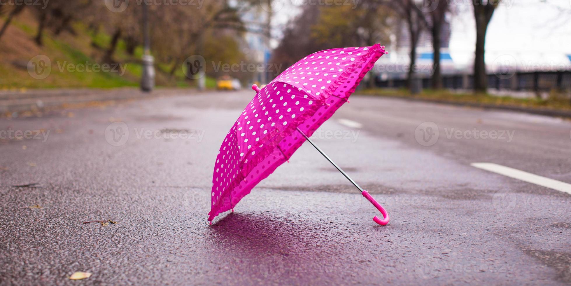 Pink children's umbrella on the wet asphalt outdoors photo