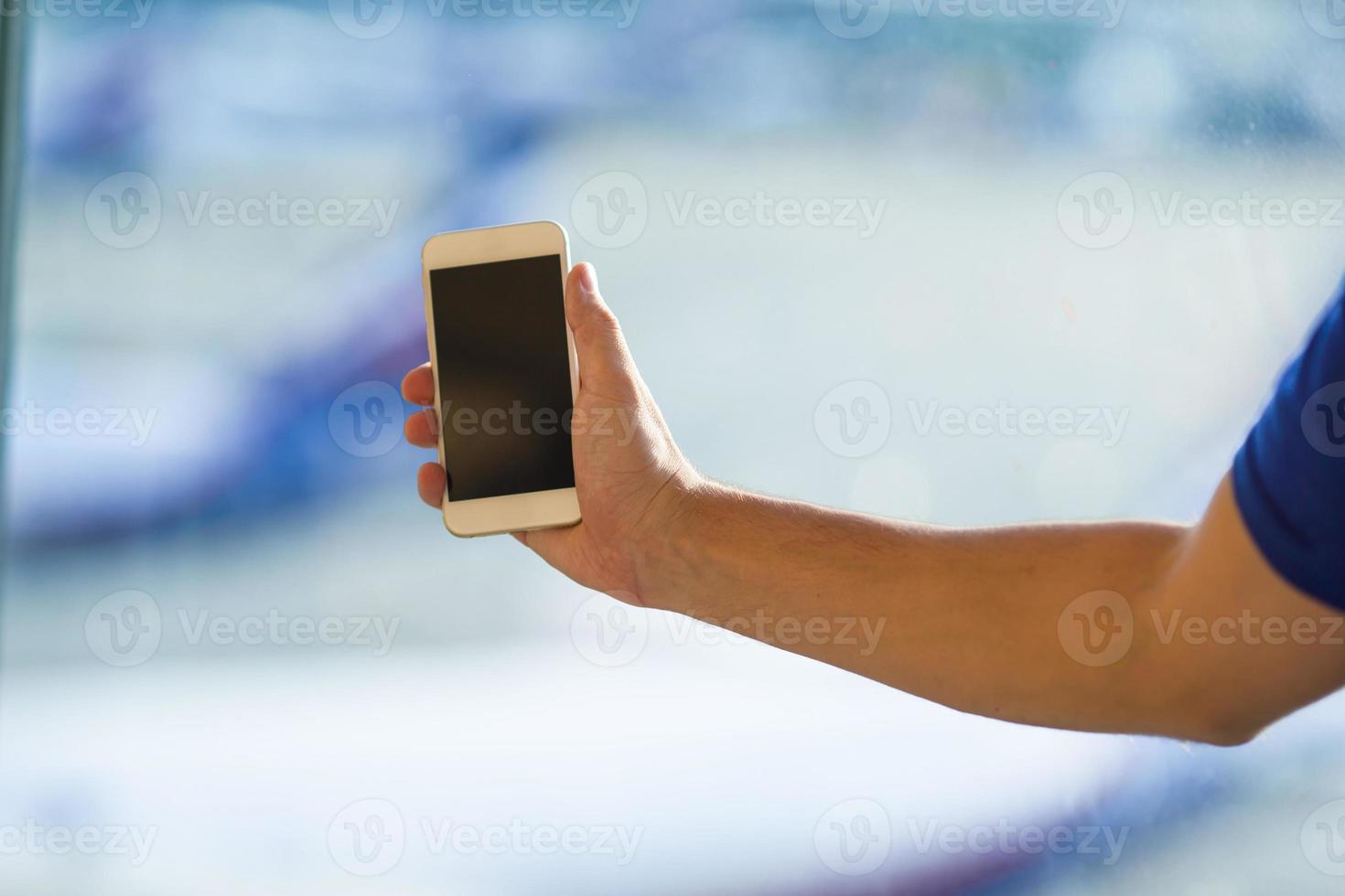 El primer plano de un joven usa un teléfono inteligente en la ventana de fondo del aeropuerto foto