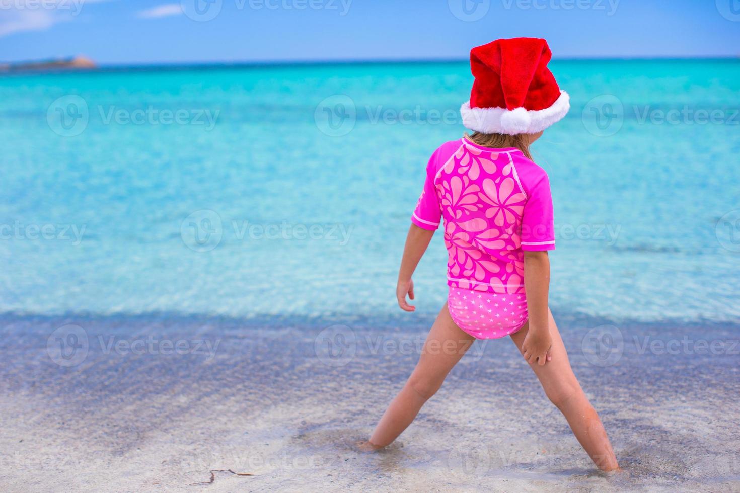 Little adorable girl in red Santa hat at tropical beach photo